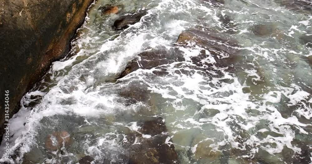 Foaming and splashing background of sea waves near a rocky shore in sunny weather Foaming and splashing background of sea waves near a rocky shore in sunny weather