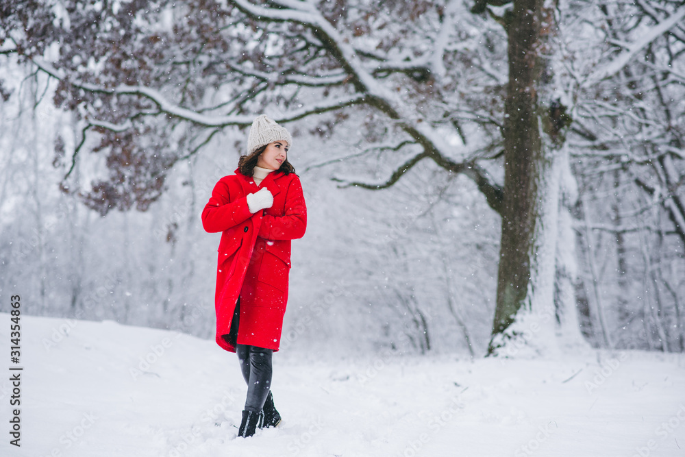 Young girl in a red coat walking in a snow-covered park. Christmas is comming. New Year. 