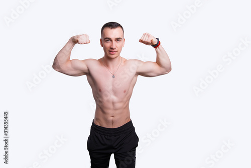 Handsome strong athletic man standing with his hands up near a white wall.