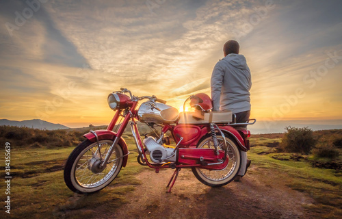 Homem junto a moto antiga a ver o pôr do sol