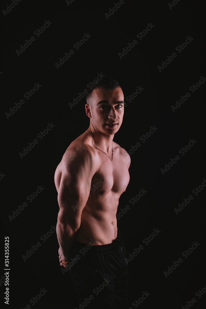Fototapeta premium Vertical portrait of muscular young man standing over dark background