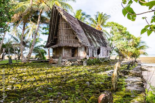 Traditional thatched yapese men's meeting house faluw or fale, a bank of megalithic stone money rai and a bunch of stone seat backs around. Shore of Pacific ocean. Yap island, Micronesia, Oceania