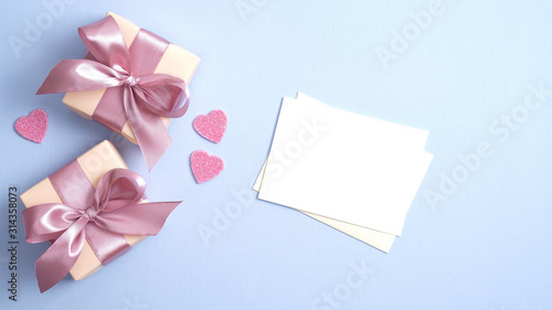 Valentine gift boxes with pink ribbon bow and romantic love letter on pastel blue background with heart shaped confetti. Valentines day banner design. Flat lay, top view.
