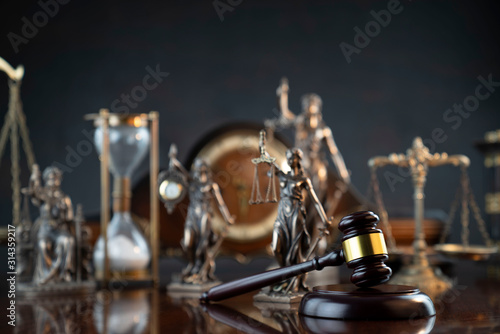 Law and justice theme. Judge’s gavel, Themis statue,  scale, hourglass and old clock on the shining wooden brown table and the gray background.