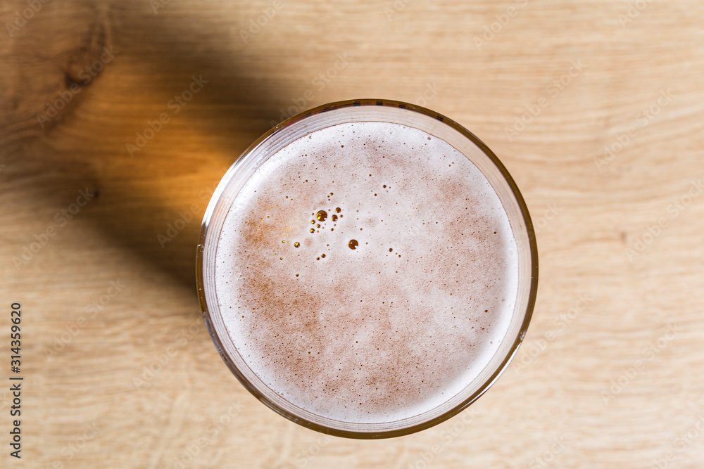 Blond beer with froth on a glass pot on a wooden board Blond beer with froth on a glass pot on a wooden board