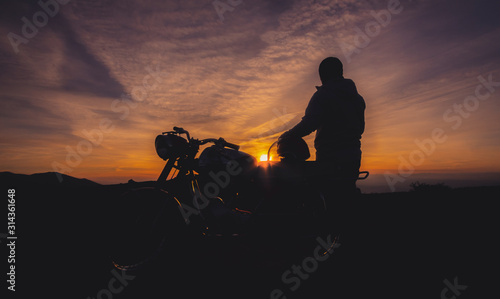 Bonita silhueta de pessoa junto a mota ao pôr do sol
