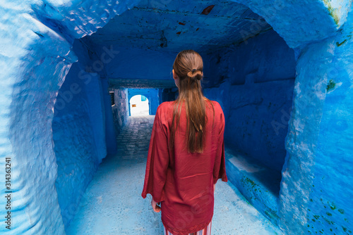 the figure of a girl in cherry-colored clothes stands in the long corridor of the blue city of Morocco © nelen.ru