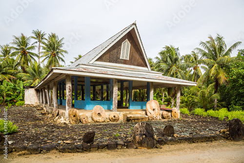 Traditional thatched yapese men's meeting house called faluw or fale and a bank of three historic megalithic stone money rai in front of it. A high coconut palm. Yap island, Micronesia, Oceania photo