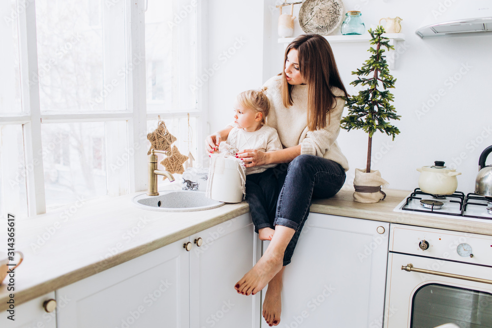 Mom feeds her daughter from a spoon. Family in the bright kitchen. Mom feeds her daughter from a spoon. Family in the bright kitchen.