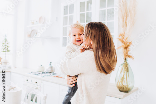 Mother and daughter in a bright kitchen. Homeliness. Joyful baby and his mom. 