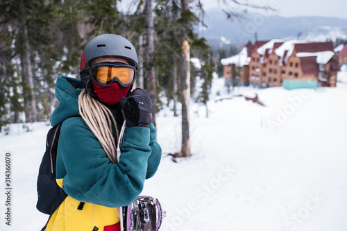 Young woman snowboarder it stands with a snowboard near the ski slopes.