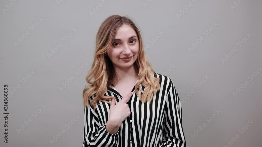 Cheerful young woman in fashion black and white striped shirt pointing finger at herself, smiling isolated on gray background in studio. People sincere emotions, lifestyle concept. Cheerful young woman in fashion black and white striped shirt pointing finger at herself, smiling isolated on gray background in studio. People sincere emotions, lifestyle concept.