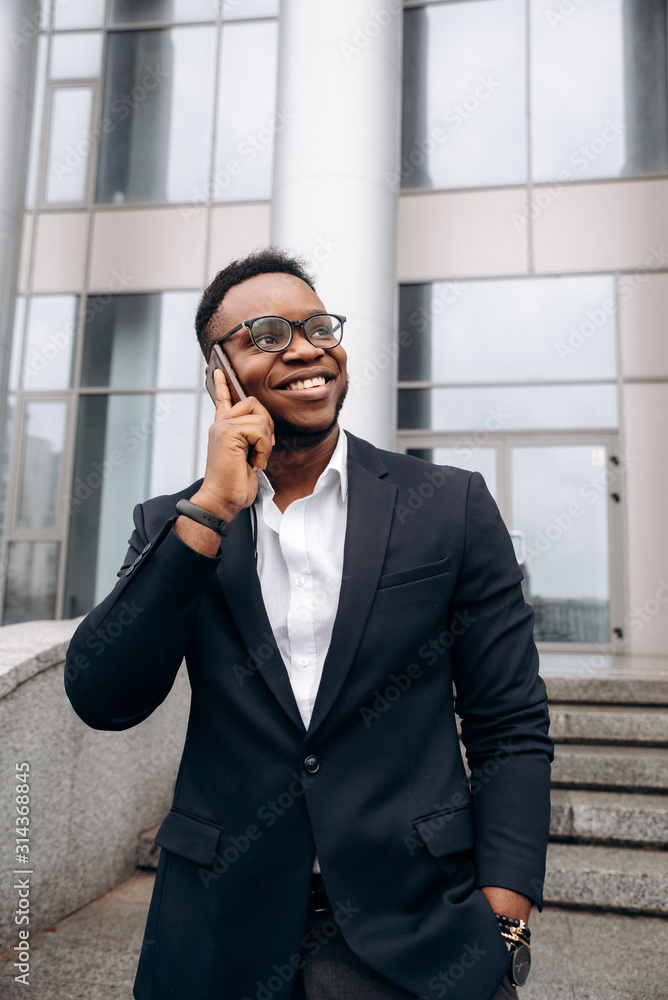 Young stylish african american man talking on the phone and smiling, near business center Young stylish african american man talking on the phone and smiling, near business center