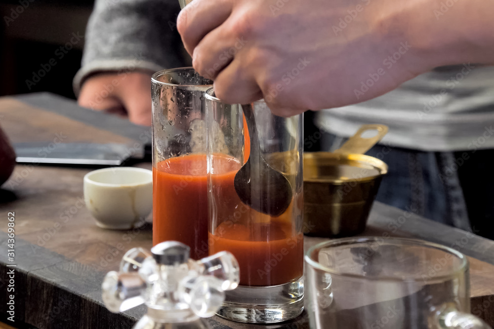 Pouring tomato juice into glasses through spoon.