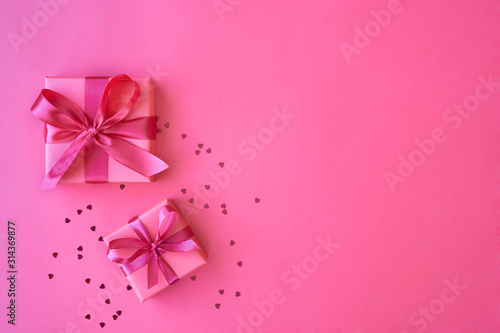 Two gift boxes with ribbon and bow on pink background with heart shaped confetti. Top view and space for text