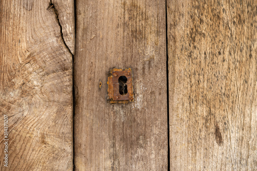 Keyhole and old metal escutcheon on a distressed grungy wooden door, close up texture view © Demianastur