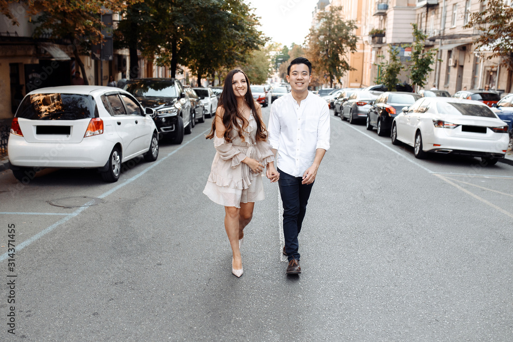 Сouple in love walks around the city. Caucasian girl and asian guy are happy together Сouple in love walks around the city. Caucasian girl and asian guy are happy together