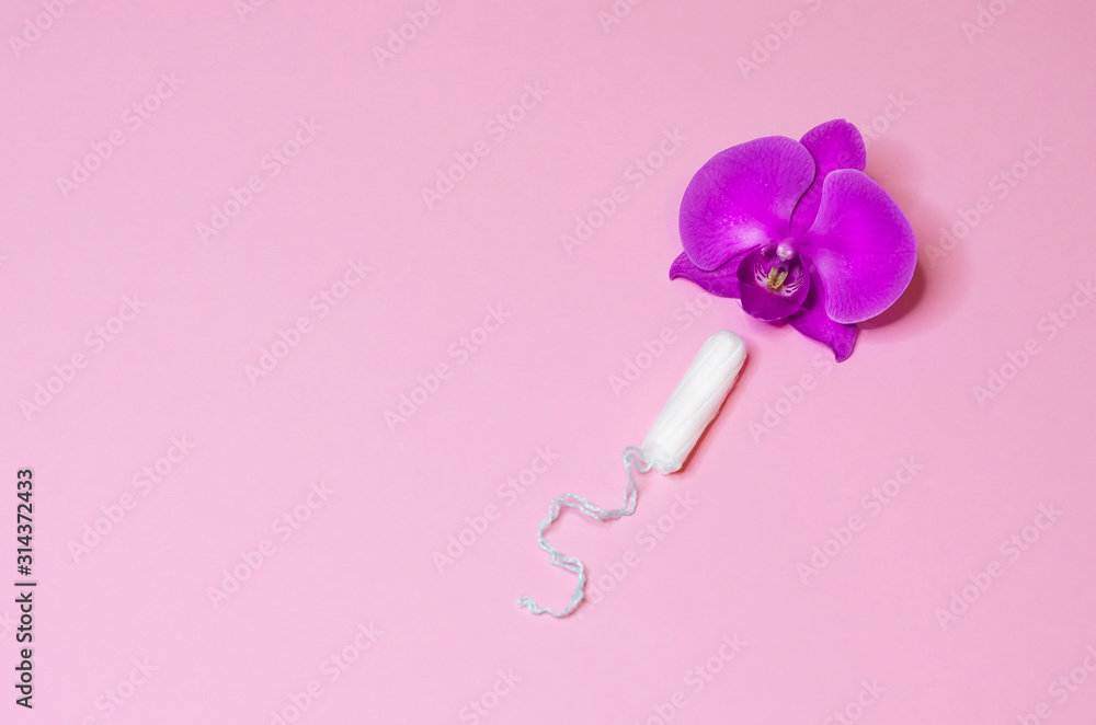 Fototapeta premium tampon as a remedy for critical menstrual days with flower orchid on pink background. hygiene, care and cleanliness of woman. copy space for text