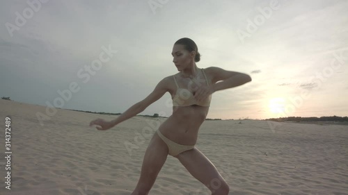 A beautiful dark hair dancer girl in a light bikini swimsuit dancing in the evening desert. Contemporary dance in the desert on the sand. Beautiful woman dancer in a swimsuit dancing.