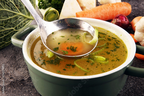 Broth with carrots, onions various fresh vegetables in a pot - colorful fresh clear spring soup. Rural kitchen scenery vegetarian bouillon stock photo