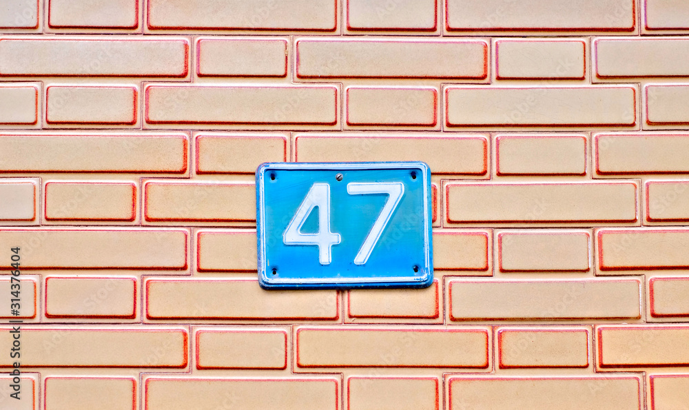 Number 47, forty-seven, a blue plate on light brown brickwork background. Number 47, forty-seven, a blue plate on light brown brickwork background.