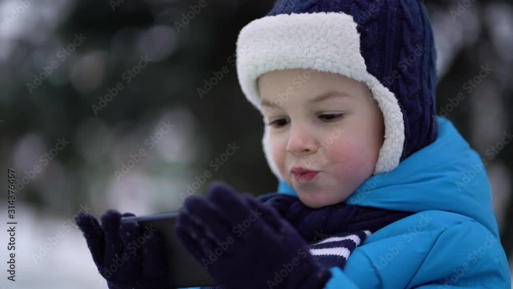 Little boy in winter wear using phone on cold snowy day Little boy in winter wear using phone on cold snowy day
