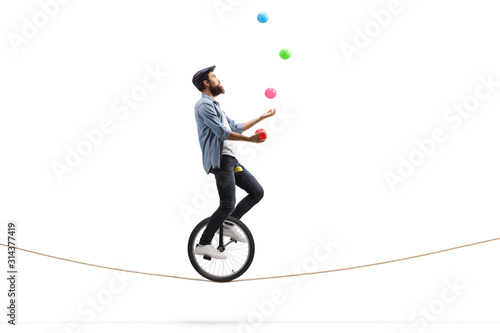Bearded male hipster juggler with balls riding a unicycle on a rope