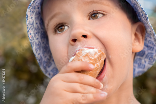 Four five year old child, boy eating ice-cream. Toddler boy eating dessert. Ice-cream in kid's hand. Child with ice-cream in cone, closeup. Boy eats ice cream