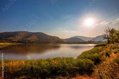 The blurred panoramic nature background of sunlight hitting the lake's surface, grass and wind blowing all the time along the large mountains, ecological beauty and fresh air.