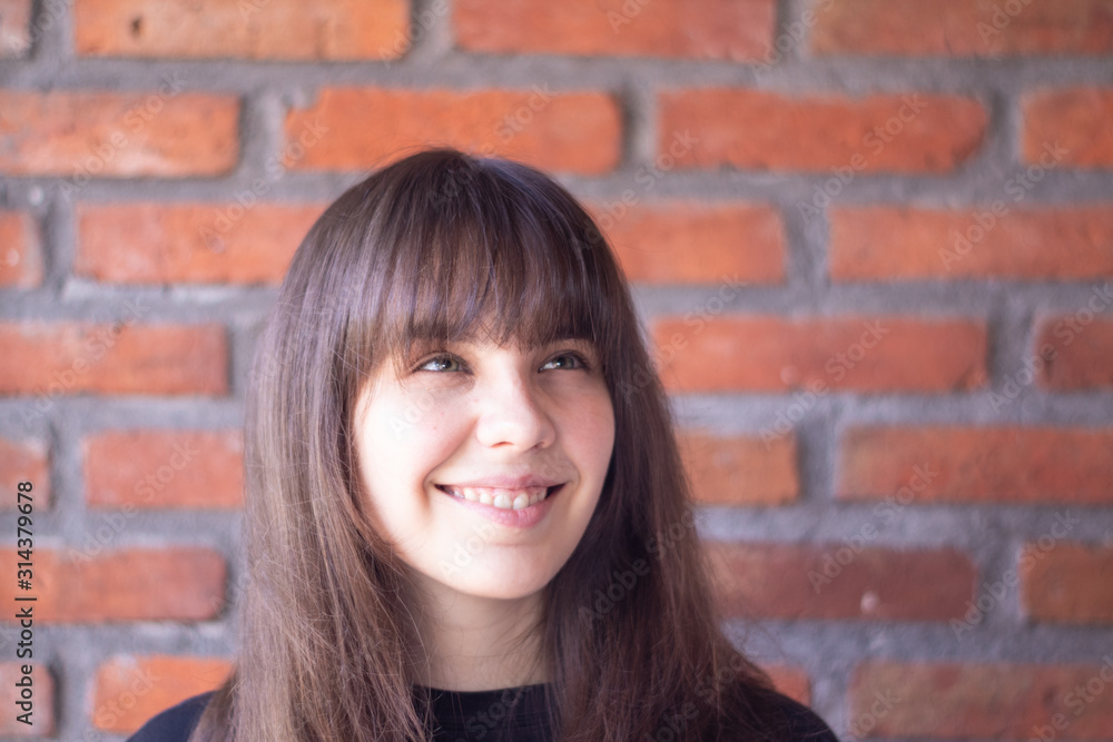 Portrait of a beautiful brunette woman with bangs wearing a black t-shirt who is happy and smiling on brick wall background Portrait of a beautiful brunette woman with bangs wearing a black t-shirt who is happy and smiling on brick wall background