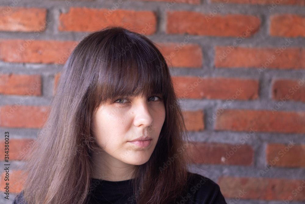 Portrait of a sad brunette woman with bangs wearing a black t-shirt on brick wall background