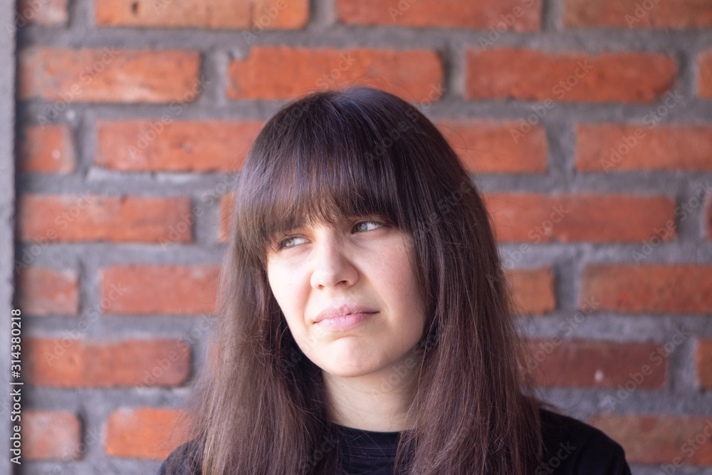 Portrait of a sad brunette woman with bangs wearing a black t-shirt on brick wall background