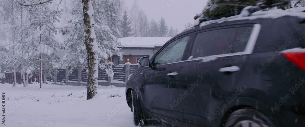 Caucasian family parking their car near the house, bringing a Christmas tree home from a shop. Snowfall, winter background. Shot on ARRI Alexa Mini w/ Atlas Orion 2x Anamorphic lenses Caucasian family parking their car near the house, bringing a Christmas tree home from a shop. Snowfall, winter background. Shot on ARRI Alexa Mini w/ Atlas Orion 2x Anamorphic lenses
