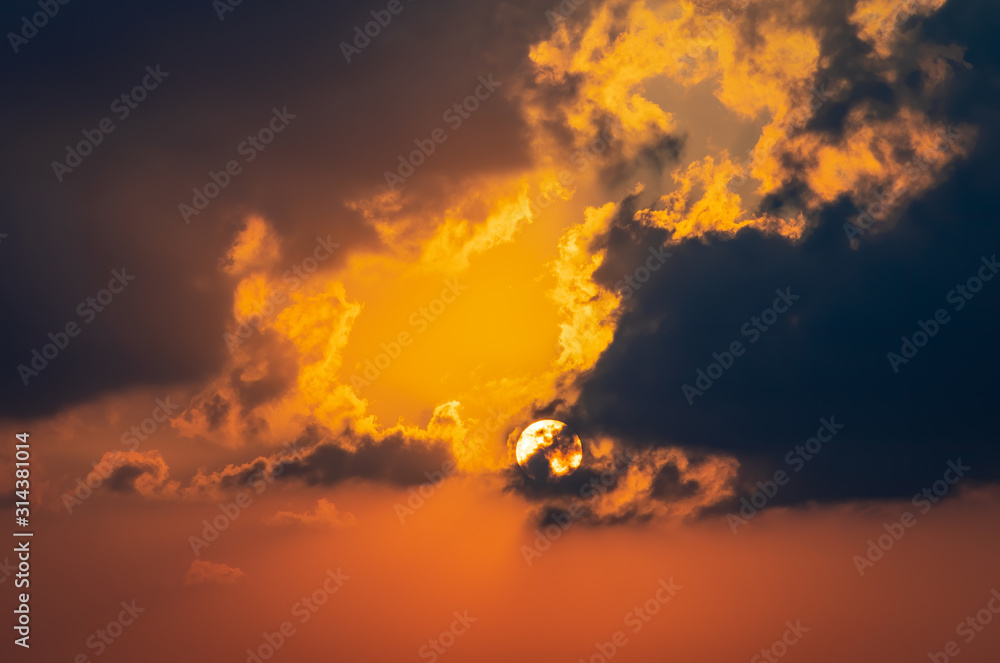 Abstract picture with the sun disappearing in the dark clouds. Red and orange sky as a background.