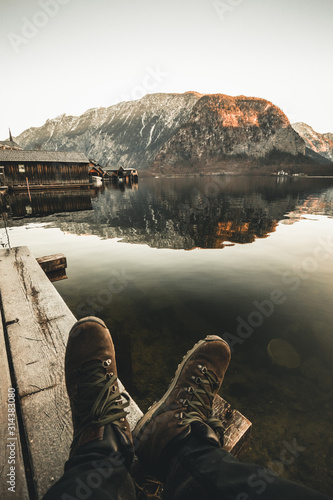 Person looking at mountain Lake Hallstatt in Austria. Boots view of a man sitting at the Pier