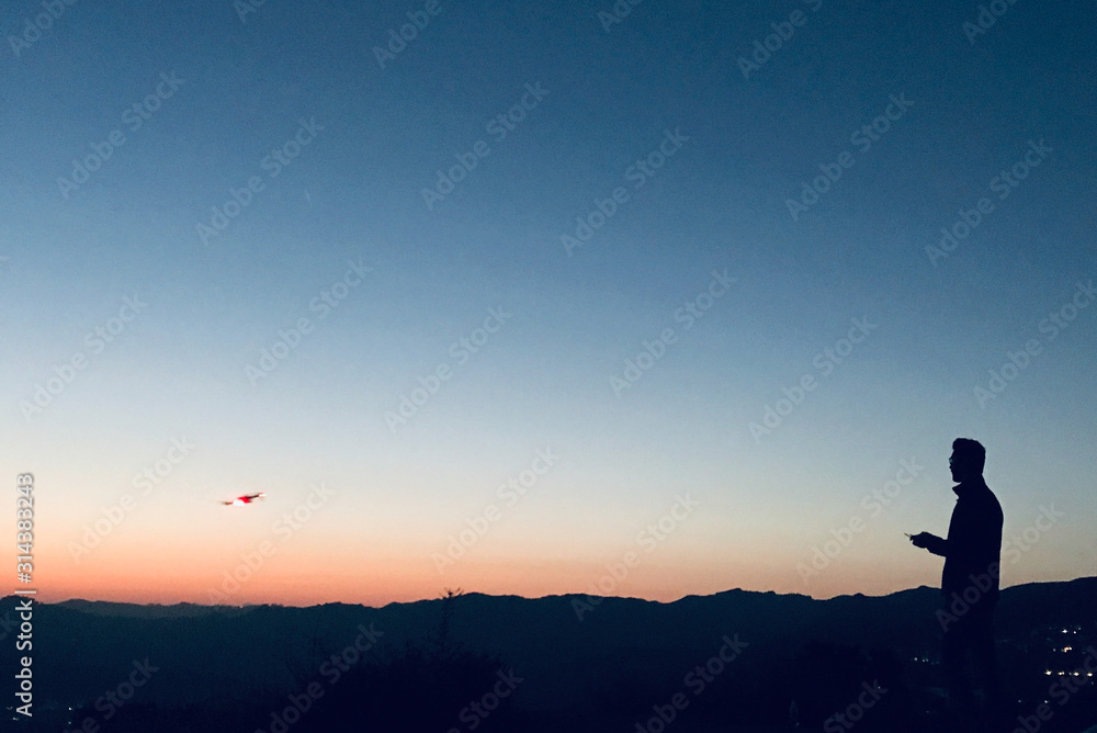 Silhouette of a man flying a drone during sunset 