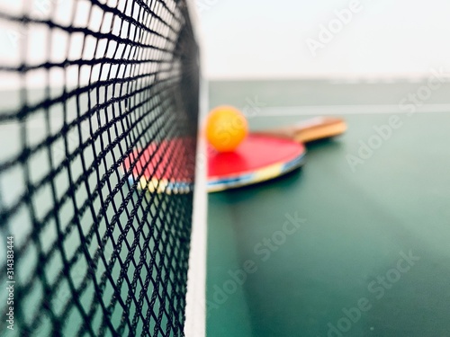 Close up of ping pong table net with ping pong ball and paddle blurred in the background