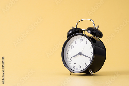Small black alarm clock in front of yellow background