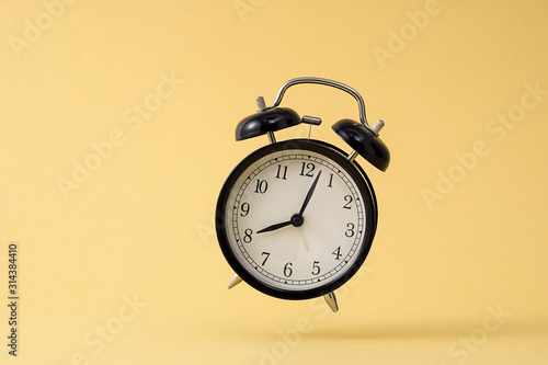 Small black alarm clock in front of yellow background