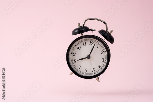 The small black alarm clock is suspended in front of the pink background.