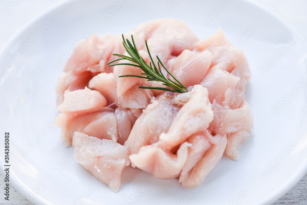 Pieces of raw chicken meat with rosemary - fresh raw cut chicken fillet on white plate background Pieces of raw chicken meat with rosemary - fresh raw cut chicken fillet on white plate background