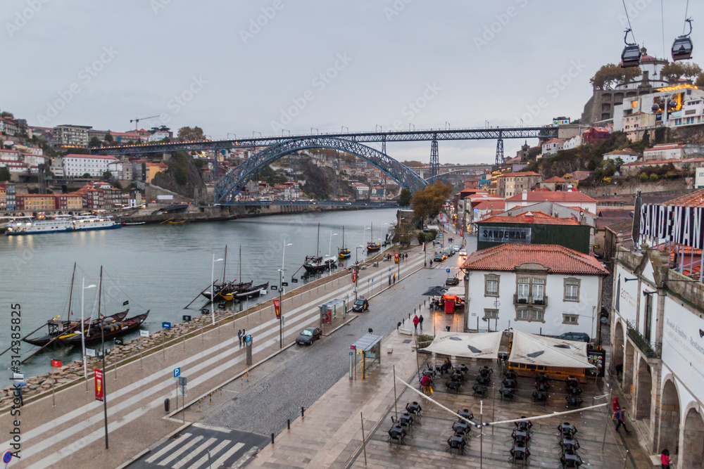 PORTO, PORTUGAL - OCTOBER 18, 2017: Dom Luis bridge over Douro river in Porto, Portugal. Port wine carrier boats on the river.