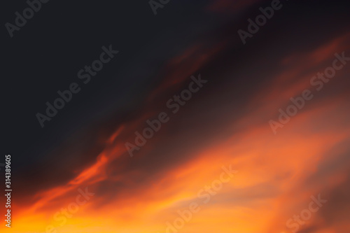Dramatic atmosphere blurry image of twilight sky and golden cloud look like fire flame on dark sky background. © ekapolsira