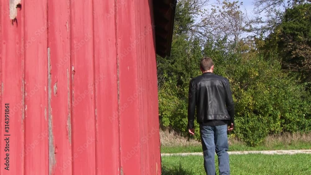 Man in black leather jacket walks besides an old red barn. The farm is located outside of Ames, Iowa. Man in black leather jacket walks besides an old red barn. The farm is located outside of Ames, Iowa.