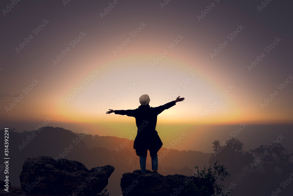 A woman watching the sunset and raising her hands up. Success concept.