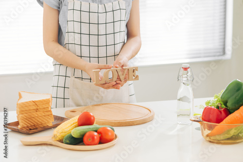 Asian woman with wooden letter LOVE at table with toast and vegetables in kitchen at home