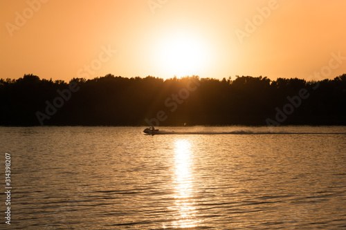 A male cruising along the river on a fast wave runner, high contrast scene of picturesque sunset.