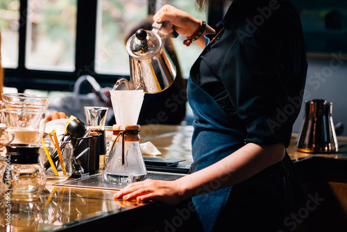 Foto Women Barista to make a drip brewing, filtered coffee, or pour-over is a method which involves pouring water over roasted, ground coffee beans contained in a filter