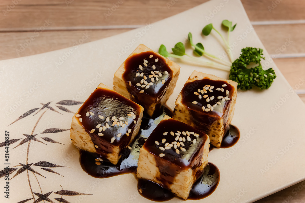Tofu no Dengaku is grilled Tofu with sesame seed and Hatcho Miso Sauce on brown plate and wooden background.