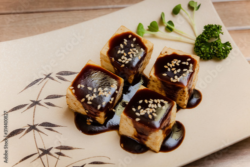 Tofu no Dengaku is grilled Tofu with sesame seed and Hatcho Miso Sauce on brown plate and wooden background. photo